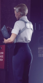 An image from quarter-rear perspective of a blonde, short-haired woman dressed in office attire standing with clipboard