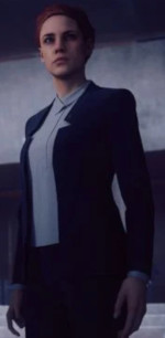 An image in quarter-front perspective of a standing red-haired woman wearing a pants-suit