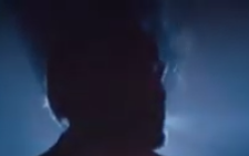 Shadowy silhouette of a man's head turned in profile as he exhales cigarette smoke on a blurry blue background